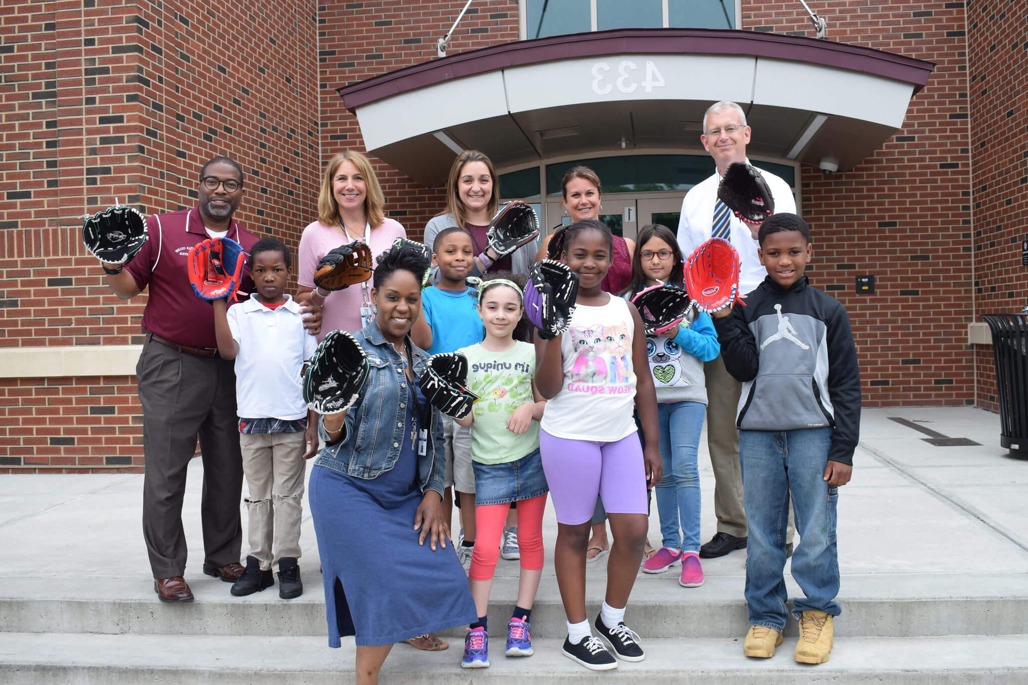 Springfield College staff stand with children on the steps, holding out baseball gloves that were just donated. 