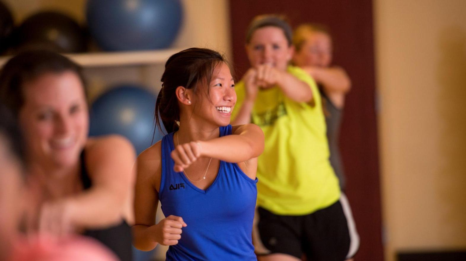 Female students smile as they work out in a group exercise class at Springfield College