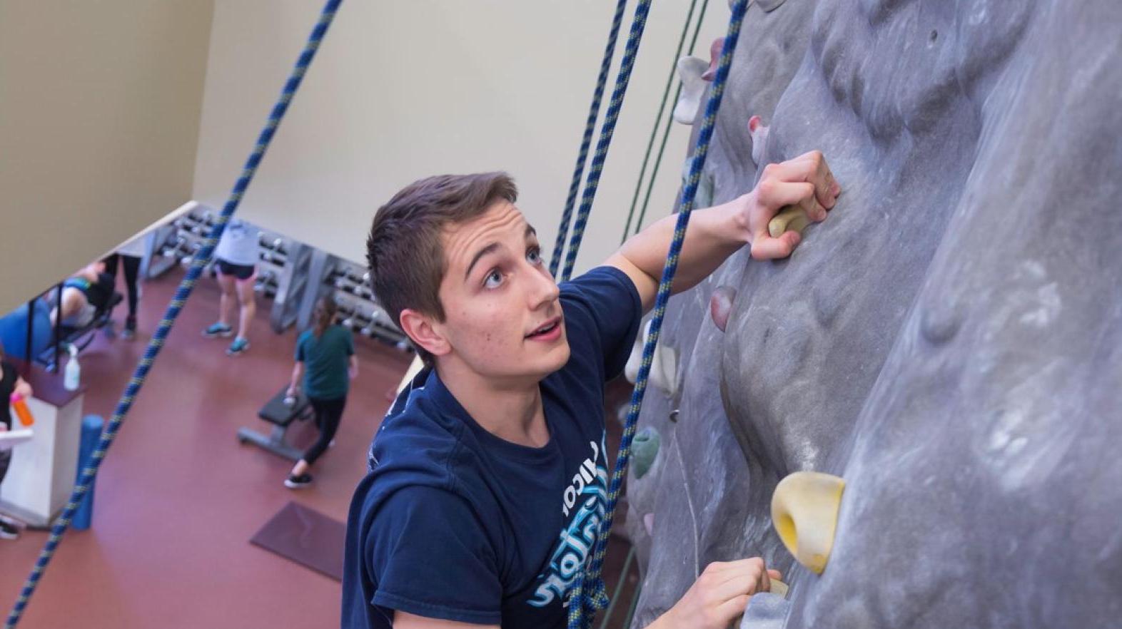 Male student using the climbing wall in Springfield College Wellness Center